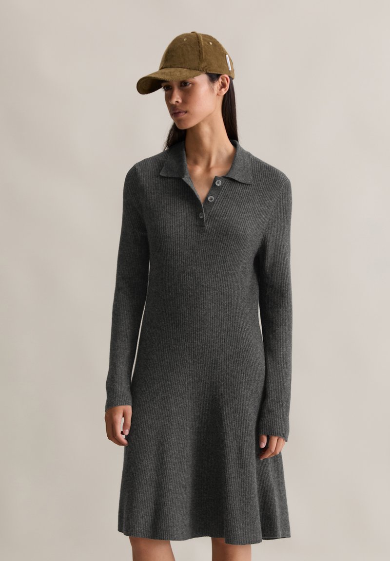 Abito grigio a coste con maniche lunghe e colletto polo, con gonna leggermente svasata. Accentuato da un berretto in corduroy marrone.