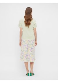 Lichtgroen shirt met korte mouwen gecombineerd met een pastelgekleurde midirok, die een patroon van paarse en gele bloemen laat zien met een vloeiende stofbeweging.