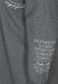 Tissu gris avec texte blanc indiquant "Chaque nouveau jour est une nouvelle opportunité de vous améliorer. Saisissez-la et profitez-en au maximum."