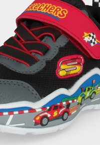 Детска черна и сива обувка Skechers с червени връзки и лепенка, с дизайн на състезателна кола и цветно лого "S" отстрани.