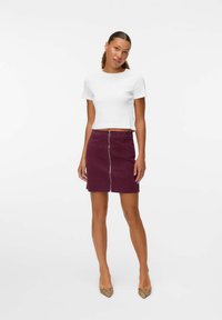 Witte cropped t-shirt, gecombineerd met een bordeauxrode corduroy mini-jurk met een centrale rits, aangevuld met beige slangenprint hakken.