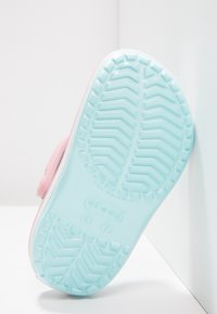 Pink footwear with a light blue, textured sole featuring a zigzag pattern and small logo. The design includes adjustable strap hardware.