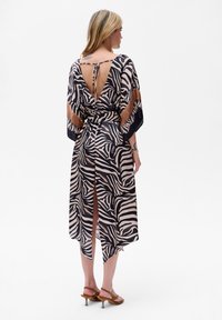 Lekka, drukowana sukienka w czarno-beżowy wzór zebra, z otwartymi plecami i wiązaniem, oraz wysokimi rozcięciami, z zwiewnymi rękawami.