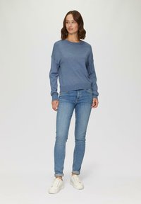 Svetlo modra pulover s dolgimi rokavi, okroglim izrezom in sproščenim fitom, v kombinaciji s svetlimi denim hlačami in belimi supergami.