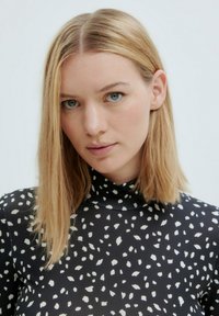Zwarte turtleneck met een wit abstract patroon, gladde stof, aansluitend ontwerp en steil blond haar.