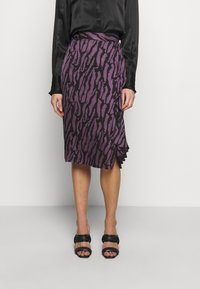 Falda de estampado animal púrpura con cintura ajustada y detalle de volantes en el dobladillo, combinada con sandalias negras y una blusa negra de satén.