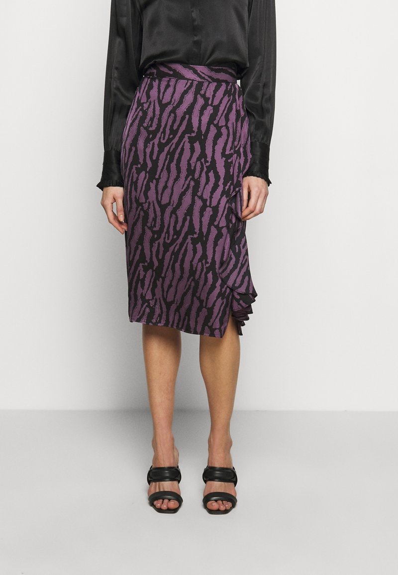 Falda de estampado animal púrpura con cintura ajustada y detalle de volantes en el dobladillo, combinada con sandalias negras y una blusa negra de satén.