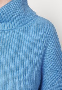 Maglione a maglia blu chiaro con collo alto a imbuto, caratterizzato da un motivo a costine testurizzato e un tessuto morbido e leggermente morbido.