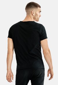 Svart kortärmad t-shirt i mjukt tyg, med en klassisk rund halsringning och avslappnad passform, visad bakifrån.