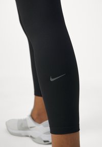 Svart leggings av elastisk tyg, med en liten grå Nike-logga på sidan och i kombination med vita träningsskor.