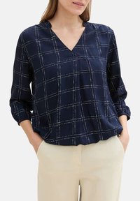 Blouse bleu marine avec motif à carreaux, décolleté en V et manches trois-quarts. Fabriquée en tissu léger avec une texture douce.