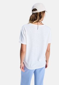 Witte t-shirt met korte mouwen, in een ontspannen pasvorm en met een ronde halslijn, gecombineerd met lichtblauwe broek. De stof heeft een zachte, gestructureerde uitstraling.