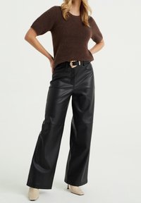 Brun texturerad stickad tröja kombinerad med svart, höga vida byxor i konstläder, accentuerade med ett mönstrat skärp och ljusa neutrala klackskor.