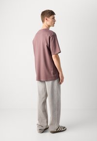 T-shirt de manga curta, com corte descontraído, em algodão mauve empoeirado. Usado com calças cinza claro e ténis verde-castanho com riscas brancas.