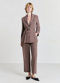 Brown tailored suit with a belted waist, notch lapels, and straight leg pants. Worn with black loafers, featuring a smooth texture.