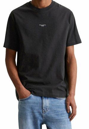 Homme portant un t-shirt noir Marc O'Polo Denim à manches courtes et un jean bleu clair, une main dans la poche, cadré au niveau du cou et des hanches.