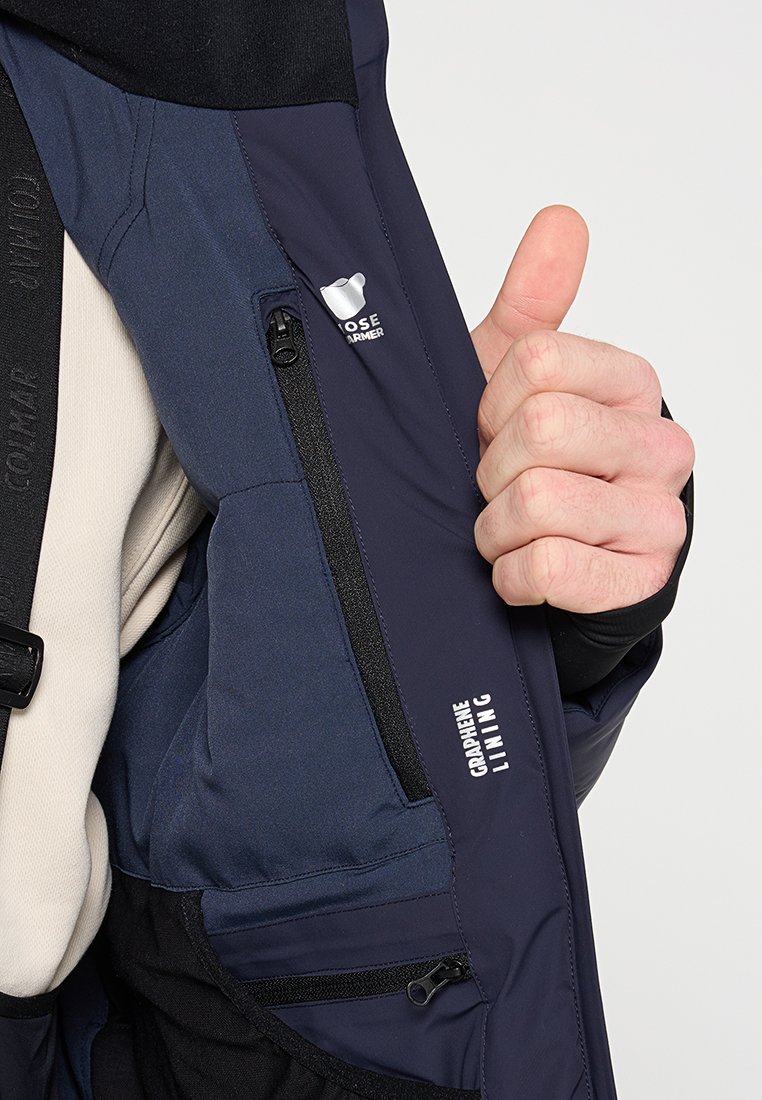 Giacca impermeabile color navy con tasca a petto con cerniera, fodera in grafene e dettagli con logo, caratterizzata da un'esterno liscio e testurizzato.