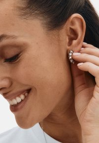 Strieborné náušnice na štuple so štvorcovým geometrickým dizajnom s tromi pyramídovými hrotmi. Povrch je hladký a lesklý, čo dopĺňa profil nositeľa.