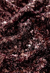 Bordeaux stof dækket af skinnende, runde paljetter, hvilket skaber et struktureret, glitrende udseende med et lagdelt, plisseret look.