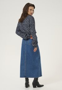 Lång denimkjol i blått, med hög midja och rak silhuett. Matchad med en mörk mönstrad blus och svarta ankelboots.