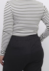 Pasiasty longsleeve w kolorze białym i oliwkowym połączony z czarnymi spodniami na elastycznej talii, które mają dwie tylne kieszenie i luźny krój.
