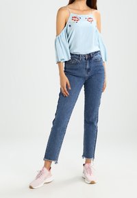 Lyseblå off-shoulder top med blomsterbroderi, parret med blå denimjeans med en frynset ankeludskæring, og lyserøde sneakers.