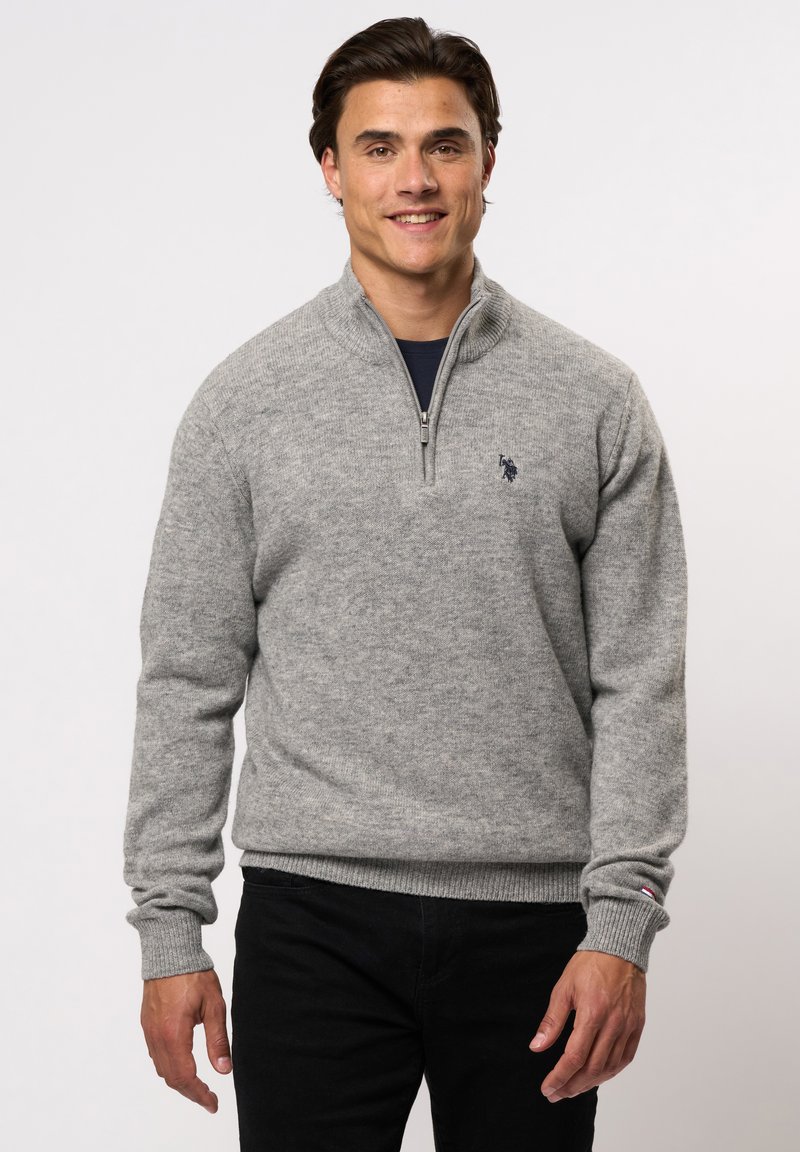 Šviesiai pilkas džemperis su užtrauktuku, pagamintas iš minkštos mezginio medžiagos. Jame yra grioveliai ant rankogalių ir apykaklės, o krūtinėje mažas tamsus logotipas. Derinamas su tamsiomis kelnėmis.