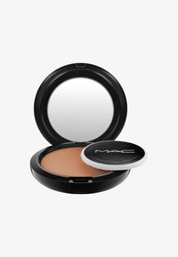 Polvo compacto de MAC con un estuche circular negro y un espejo. En su interior hay un polvo color beige y un aplicador con tapa negra y borde blanco.