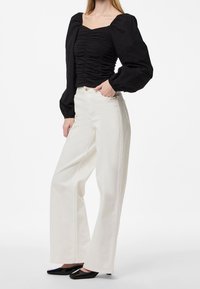 Haut noir froncé avec encolure carrée et manches bouffantes, associé à un pantalon blanc taille haute à jambes larges et des chaussures noires à bouts pointus.