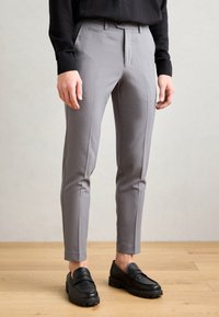 Gray tailored trousers with a slim fit, smooth fabric, dual front pleats, side pockets, and a clean waistband, paired with black loafers.