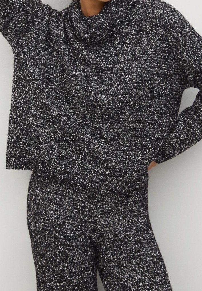 Femme portant un pull en maille texturée noir et blanc à épaules tombantes et un pantalon en maille assorti, posant avec une main sur la hanche.