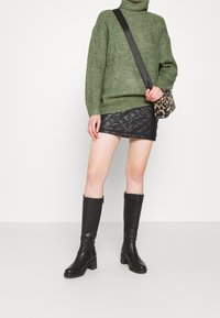Pull à col roulé en tricot vert, mini jupe en cuir matelassé noire, bottes à talons montantes noires et petit sac bandoulière en imprime léopard.