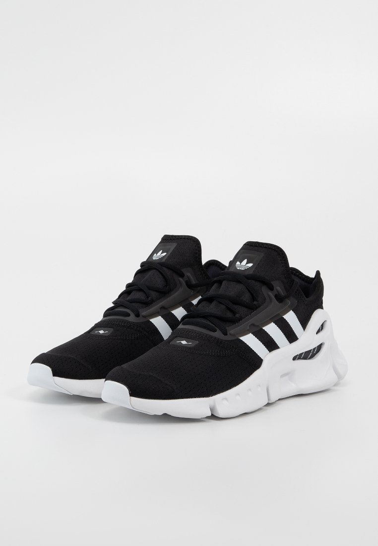 Ett par svarta Adidas-sneakers med vita ränder och tjocka vita sulor, placerade sida vid sida på en enkel vit bakgrund.