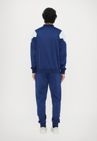 Tuta sportiva navy composta da una giacca con accenti azzurri sulle spalle e pantaloni abbinati, realizzata in un tessuto leggero e morbido.