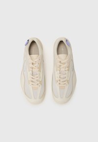 Helle beige Sneakers mit Netzpaneelen, runder Zehenpartie und Schnürsenkeln. Verfügt über einen kleinen lila Akzent an der Ferse und eine Markenkennzeichnung an der Seite.