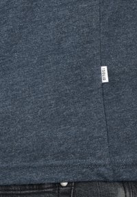 Camiseta azul oscuro de tejido texturizado, con una pequeña etiqueta blanca que dice "ISOLID" en la costura lateral, con bordes rematados.