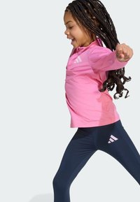 Růžové dlouhé sportovní tričko s třemi bílými pruhy na levé hrudi, v kombinaci s námořnickými legínami s bílým logem na stehně.