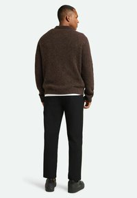 Brun striktrøje med afslappet pasform, høj krave og lange ærmer, parret med sorte bukser og sorte sneakers. Struktureret stofdetalje.