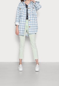 Blau-weiß kariertes, übergroßes Hemd-Jacke mit zwei Brusttaschen, kombiniert mit hellgrünen, schmal geschnittenen Hosen und weißen Sneakers.