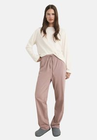 Maglietta a maniche lunghe color crema con un fit rilassato, abbinata a pantaloni rosa con coulisse. Le pantofole grigie completano l'outfit casual. Tessuto morbido.