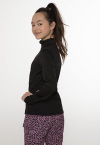 Haut noir à manches longues avec un col montant, associé à un pantalon en imprimé léopard rose. Le matériau semble lisse et extensible, avec une coupe ajustée.