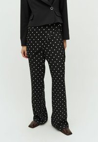 Čierne nohavice s puntíkami a voľným strihom, s drapovaným predným dielom a širokými nohavicami, doplnené hnedými topánkami s špicatou špicou.