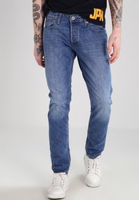 Blaue Jeans im gerade geschnittenen Stil, mit vorderen Taschen, leichter Ausbleichung und klassischer Fünf-Taschen-Optik, kombiniert mit weißen Sneakers.