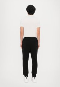 Balta polo marškinėliai su geltona apdaila, derinami su juodomis sportinėmis keln�ėmis. Modelis dėvi baltus sportbačius. Fonas baltas.