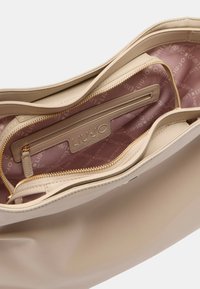 Borsa a mano in pelle beige con zip dorata, aperta per rivelare una fodera in tessuto rosa e una tasca interna con zip etichettata "Liu Jo Milano."