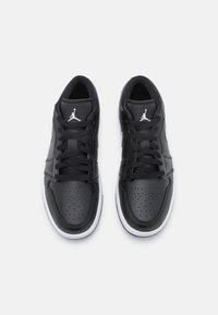 Ett par svarta och vita Air Jordan-sneakers med snören knutna, vy ovanifrån på en enkel vit bakgrund.