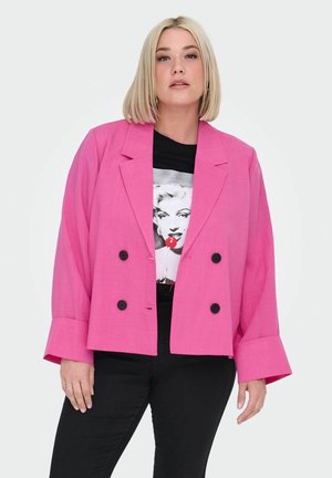 Růžový dvouřadý blazer s černými knoflíky, širokými rukávy a strukturovaným střihem, nošený přes černé tričko s potiskem a džíny.