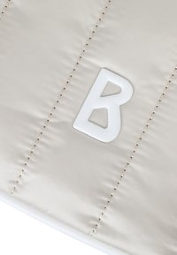 Béžová polstrovaná tkanina s lesklou texturou má výrazné bílé embosované písmeno "B" a viditelné švy.
