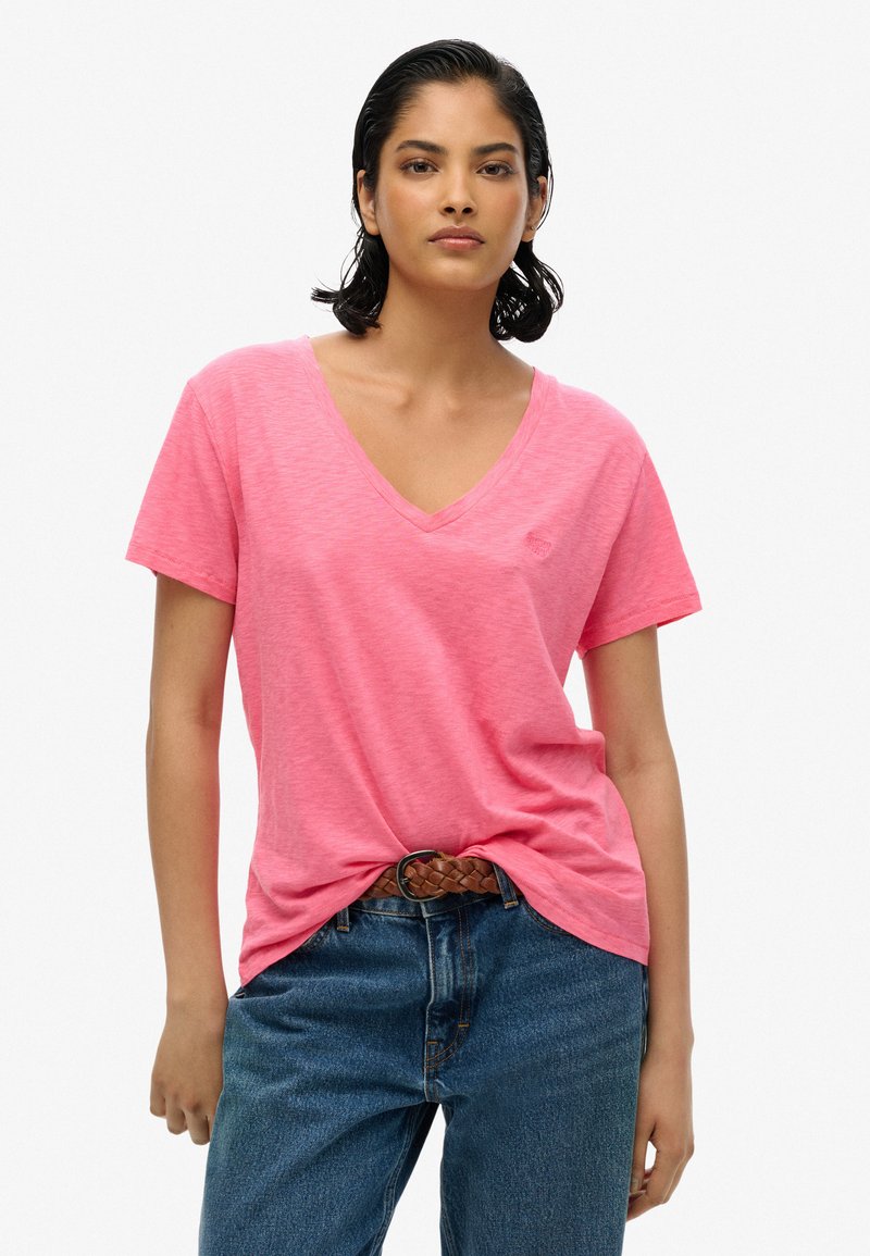 Camiseta rosa de cuello en V hecha de tela suave, corte holgado con mangas cortas, combinada con jeans de denim azul de cintura alta y un cinturón trenzado marrón.