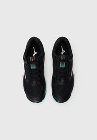 Black athletic shoes feature a mesh upper, synthetic overlays, and a green accent on the tongue. The sole is textured with orange detailing.